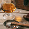 Cuban cigar and a glass of cognac brandy on wooden background, closeup view