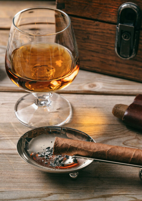Cuban cigar and a glass of cognac brandy on wooden background, closeup view